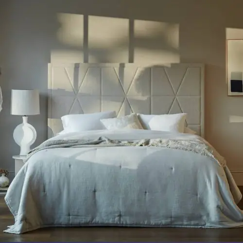 A beautifully made bed featuring the Vispring Luxury Beds, crafted with natural materials and showcasing expert craftsmanship for a truly luxurious sleep experience. The bed is set in a stylish room with sunlight streaming in, highlighting the high-quality bedding and elegant design.