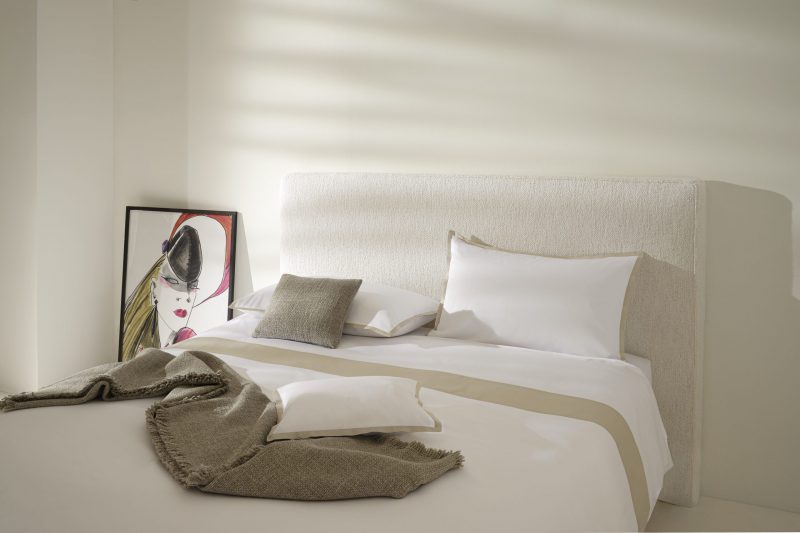 white bed sheet with four pillows in a bed with painting of a girl on the side table