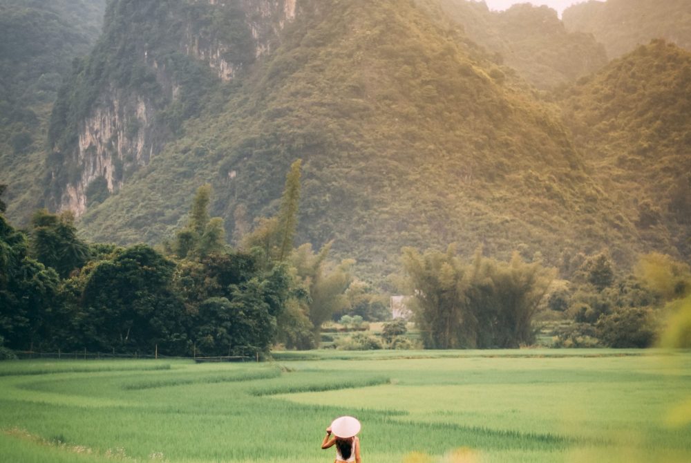 girl with a hat facing the field with a background of mountains